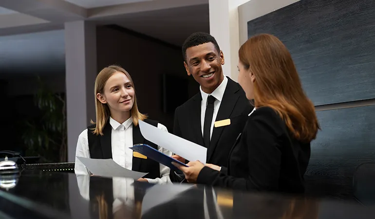 Dos recepcionistas de hotel sonríen mientras revisan documentos con una compañera junto al mostrador