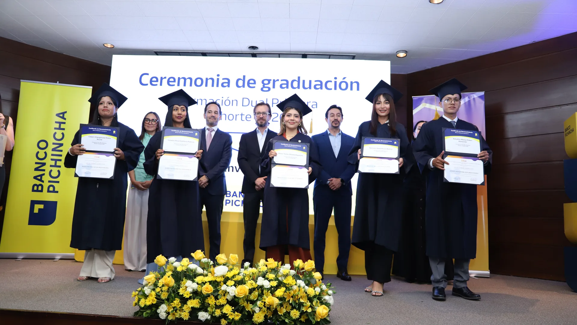 Graduados de la primera cohorte de Microfinanzas posan en el escenario con sus certificados, junto al banner de Banco Pichincha